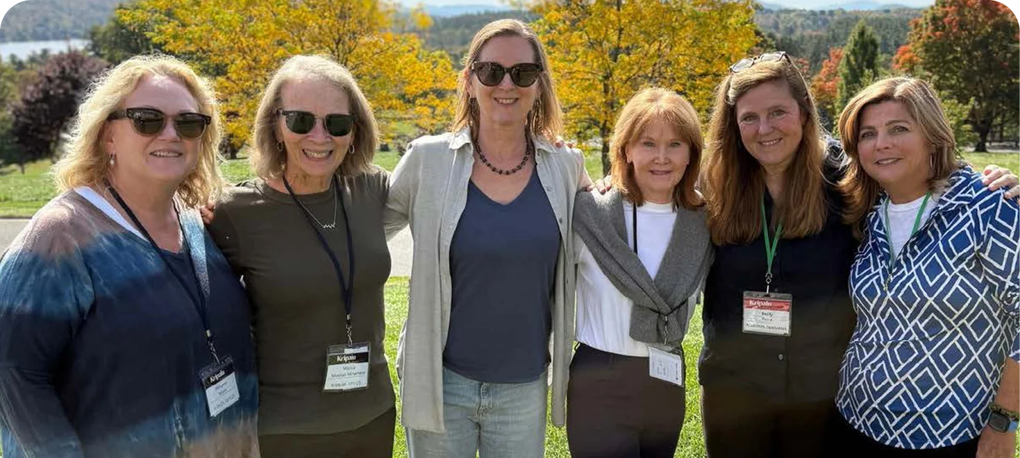 Six women wearing name badges pose together outdoors at a 911 wellness event in autumn