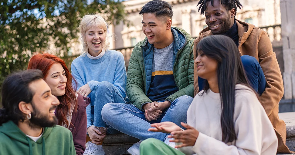advance global solidarity Diverse group of young people laughing and talking together outdoors on campus steps.
