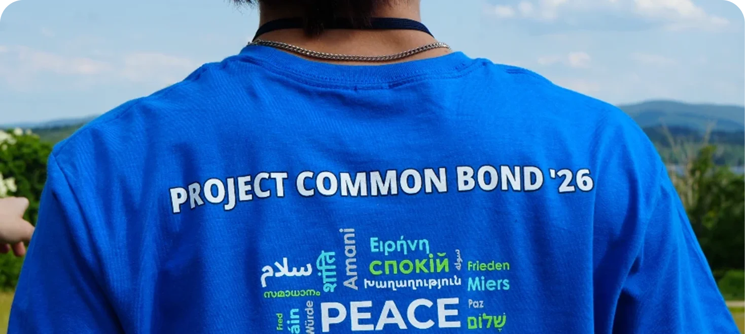 Person wearing a blue Project Common Bond '26 t-shirt with 'peace' in multiple languages