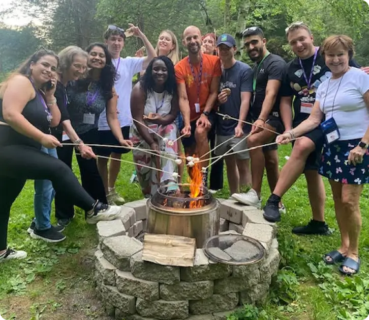 dia 2 1x Group of people roasting marshmallows together around an outdoor stone fire pit