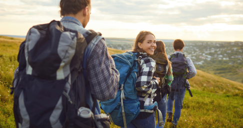 image 2 1x Group of friends hiking on a green hillside with backpacks at sunset