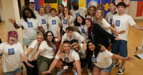 image 3 1x Large group of smiling young people in matching white T-shirts posing together with international flags behind them.