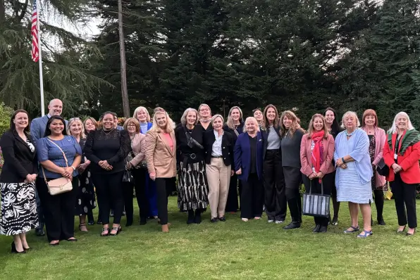 Large group of professionals posing outdoors on a lawn with an American flag and evergreen trees