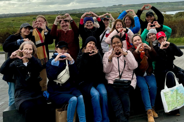 image 9 Group of women making heart shapes with their hands outdoors with scenic countryside behind them.