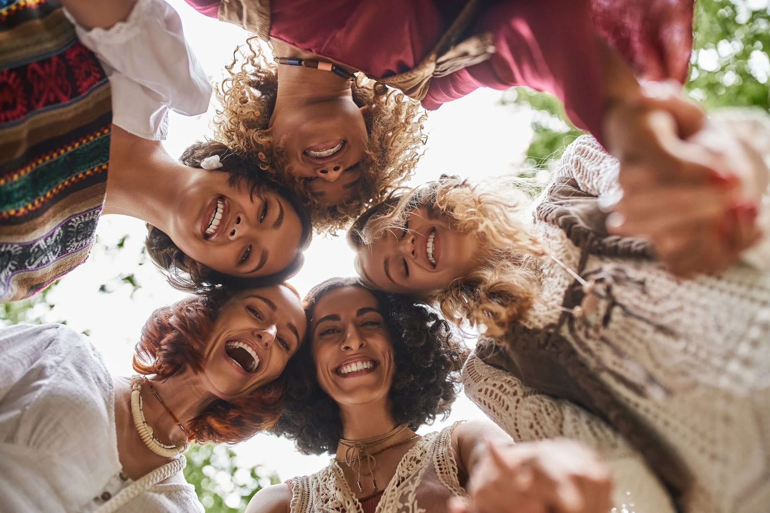 A low-angle shot of five diverse women holding hands in a circle, laughing and looking down at the camera.