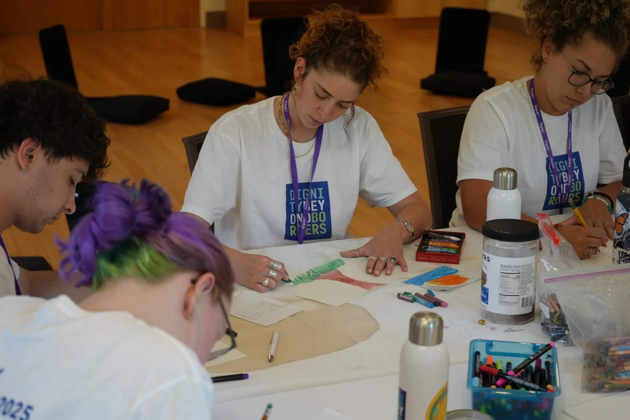 Young adults wearing matching t-shirts focusing on drawing and coloring during an art session.