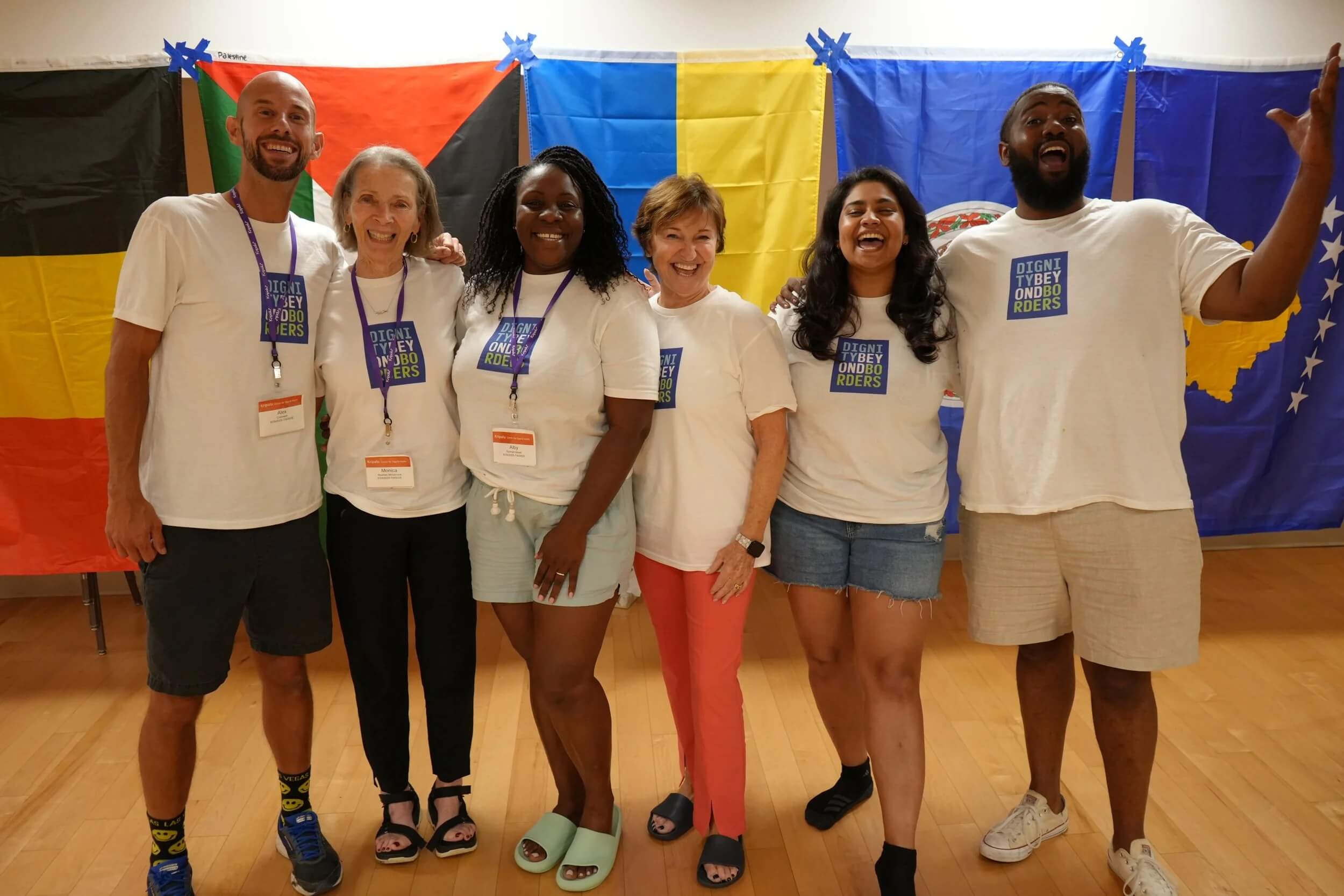 Six team members laughing and posing arm-in-arm in front of colorful international flags.