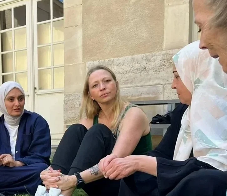 Four women sitting together outdoors in conversation near a stone building.