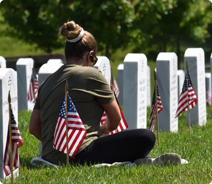 Woman sitting at a military grave with American flags at a national cemetery