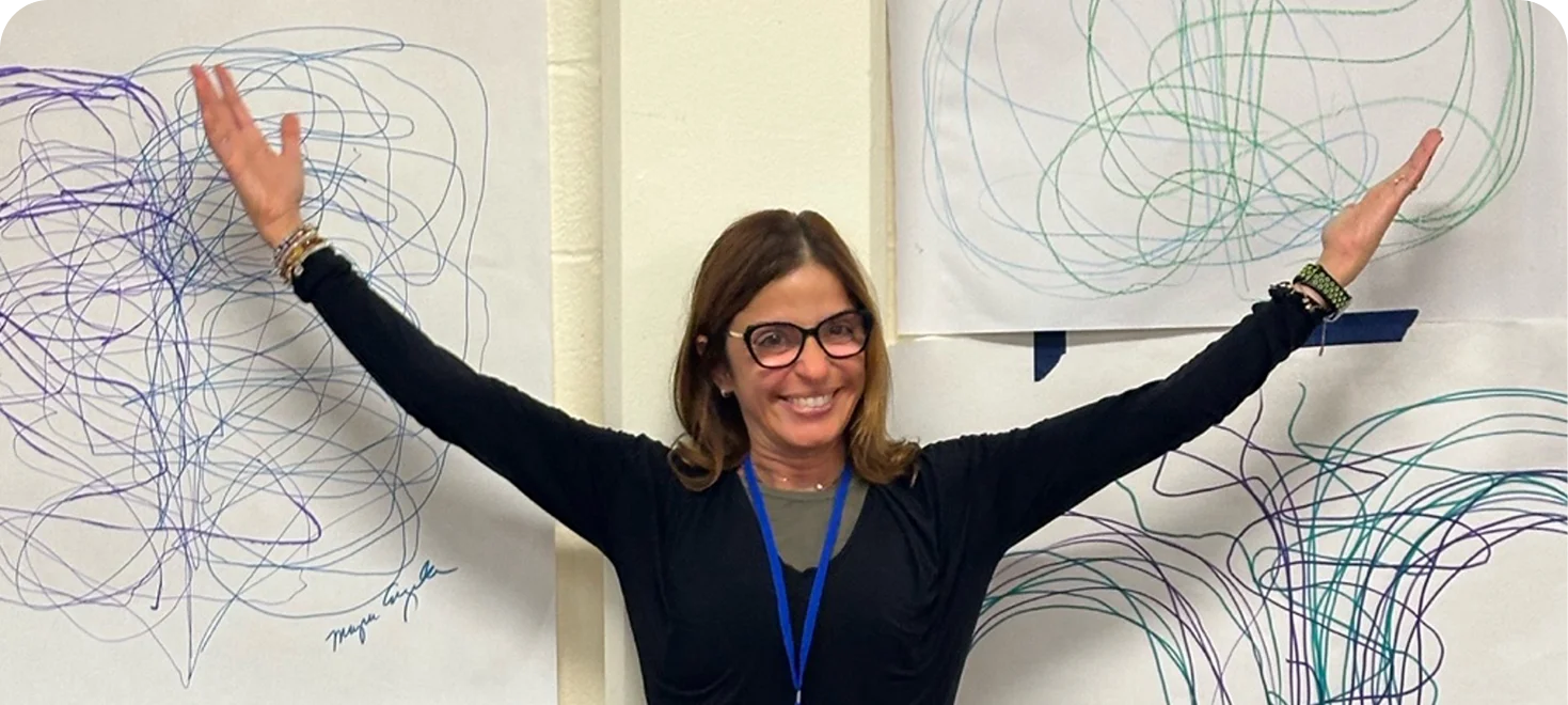 Smiling woman with arms outstretched beside large abstract scribble drawings on paper