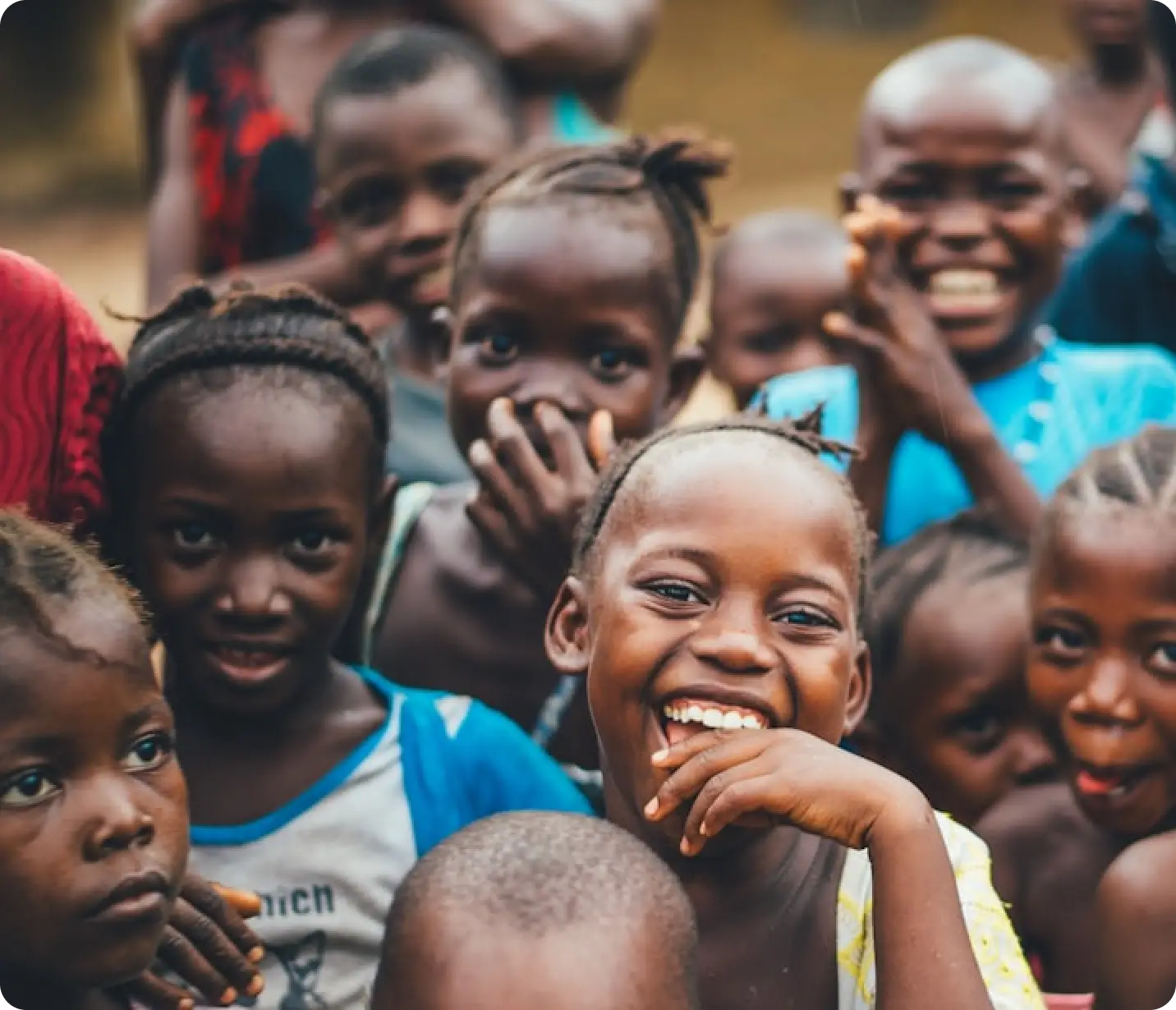 A group of children gathered closely together, with one young girl in the front laughing and smiling brightly.