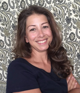 Odette Helou smiling with arms crossed in front of a patterned background
