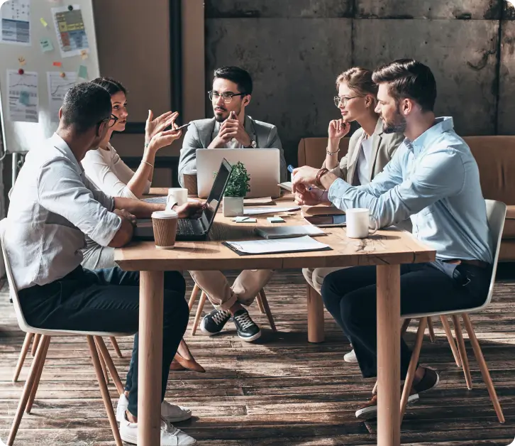 Five professionals collaborating around a table with laptops during a team meeting