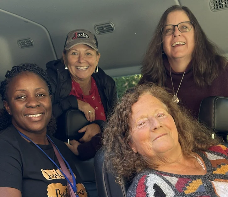 Four smiling women seated together inside a vehicle, sharing a joyful moment.